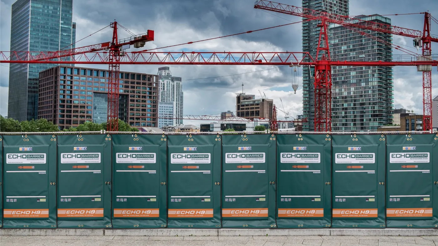 A row of green Echo Barrier acoustic barriers along a city construction site